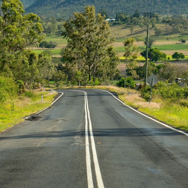 A rural road stretching into the distance with fields on either side.