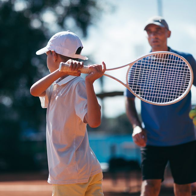 Child playing tennis under coach supervision.